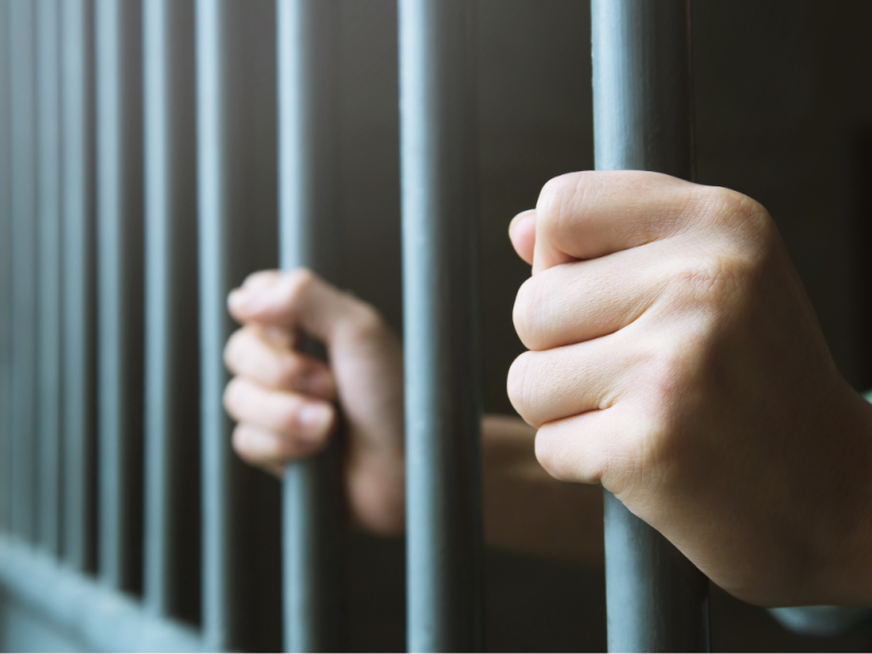 Fotografía de unas manos sujetando la reja de una cárcel