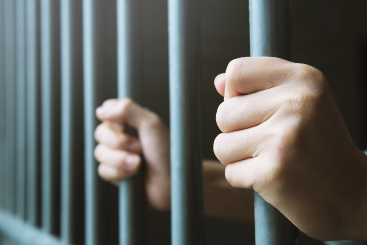 Fotografía de unas manos sujetando la reja de una cárcel